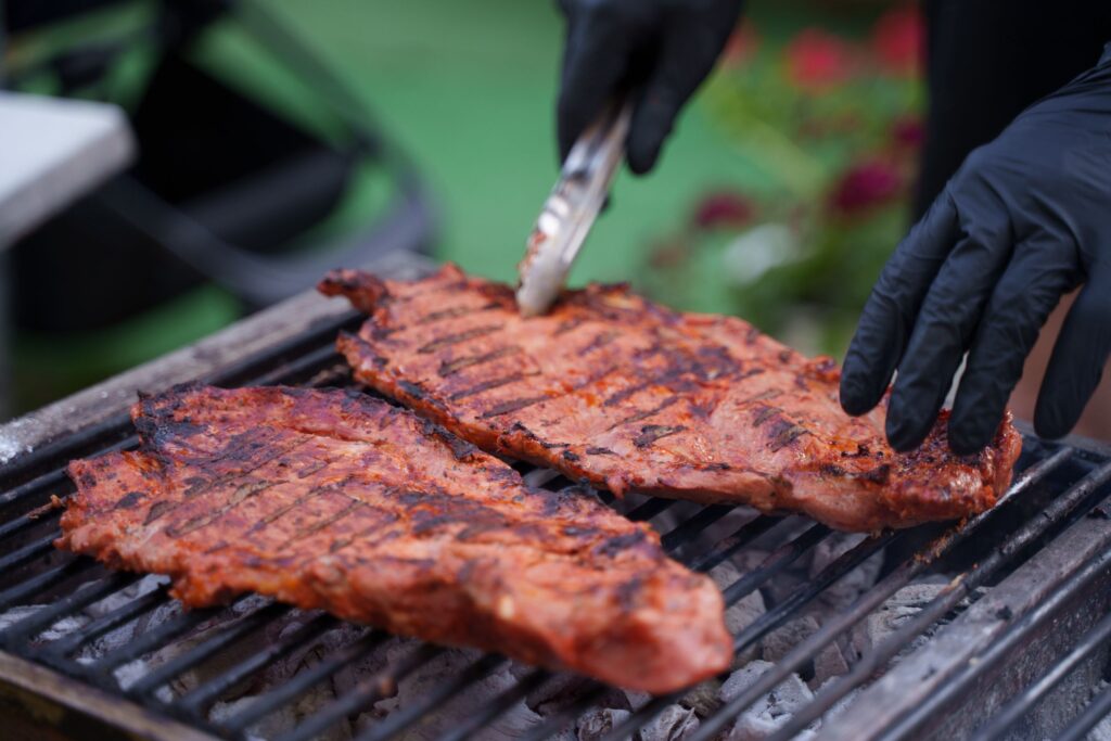 Close-up of juicy steaks grilling on an outdoor barbecue with gloved hands flipping meat.